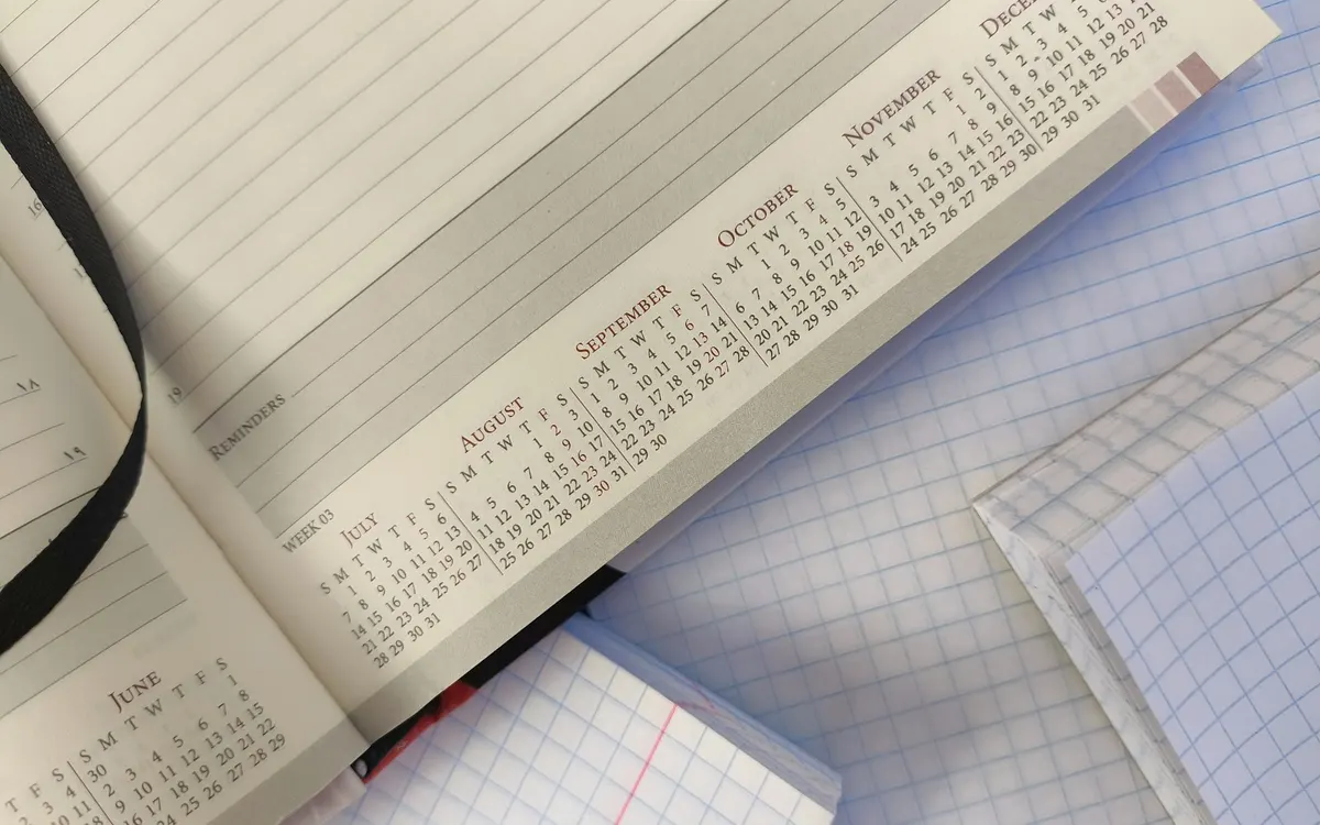 Agenda abierta con calendario y cuaderno cuadriculado sobre un escritorio